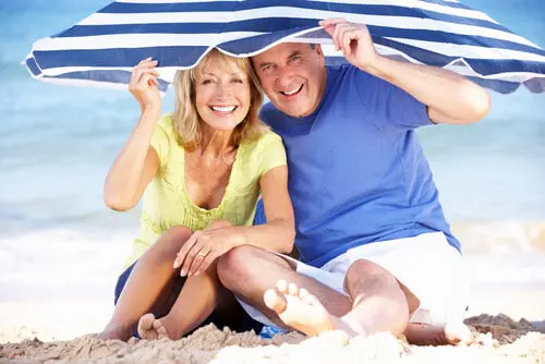 An older couple sitting on a beach under a striped umbrella